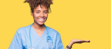 Genç Afro-Amerikan doktor kadın neşeli sunulması ve kameraya bakarak avucunun ile işaret gülümseyen izole arka plan.