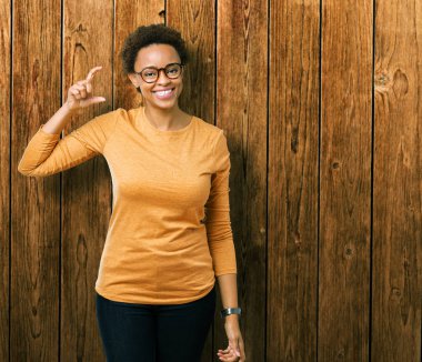 İzole arka plan gülümseyen ve süre seyir ve kamera boyutu işaret parmaklarıyla yapıyor el ile kendinden emin eller üzerinde gözlük takan genç güzel Afrikalı-Amerikalı kadın. Ölçü kavramı.