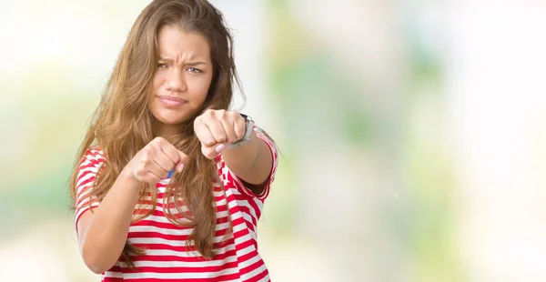 Young beautiful brunette woman wearing stripes t-shirt over isolated background Punching fist to fight, aggressive and angry attack, threat and violence