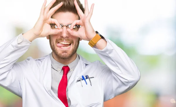 年轻英俊的科学家戴眼镜做了确定的手势 就像双筒望远镜伸出舌头 眼睛透过手指看 疯狂的表达 — 图库照片
