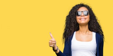 Genç güzel kız kıvırcık saçlı hareketi el ile mutlu yaşasın yapıyor moda güneş gözlüğü takıyor. Kameraya bakarak başarı gösteren ile ifade onaylama.