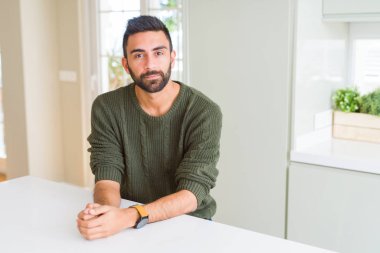 Yakışıklı İspanyol adam yüzünde ciddi ifade ile evde rahat kazak giyiyor. Kameraya basit ve doğal bir bakış.