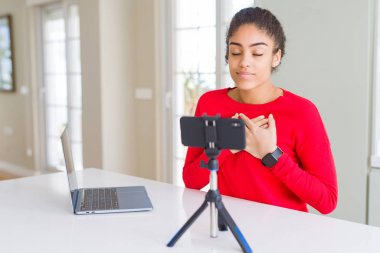 Genç Afro-Amerikalı kadın akıllı telefon kamerasıyla video çekiyor. Elleri göğsünde, gözleri kapalı gülümsüyor ve yüzünde minnet ifadesi var. Sağlık kavramı.