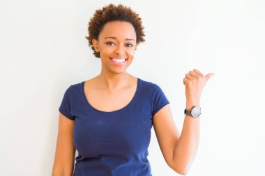 Beyaz arka plan seyir ve başparmak yanında yukarıyı mutlu yüz ile gülümseyen genç güzel Afrikalı-Amerikalı kadın.