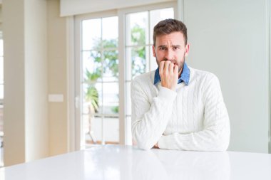 Rahat kazak giyen yakışıklı adam stresli ve sinirli ağız tırnakısırma elleri ile bakıyor. Anksiyete sorunu.