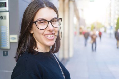 Şehir sokaklarında yürürken heyecanlı gülümseyen güzel genç esmer kadın, şehirde açık havada mutlu ve güven ifade ayakta