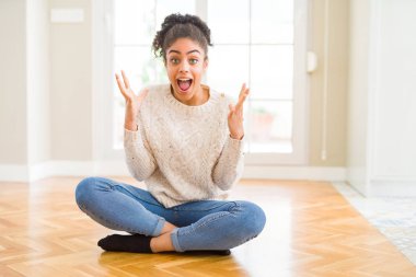 Afro saç ile güzel genç Afrikalı Amerikan kadın yerde oturan çılgın kutluyor ve başarı için hayran silah ile yükseltilmiş ve açık gözleri heyecanlı çığlık. Kazanan kavramı