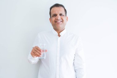 Orta yaş adam ayakta mutlu bir yüz ile beyaz arka plan üzerinde bir bardak su içme ve dişleri gösteren kendinden emin bir gülümseme ile gülümseyerek