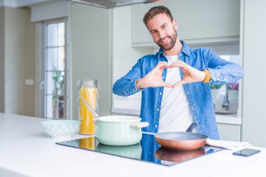 Yakışıklı adam mutfakta İtalyan spagetti makarna pişirme sevgi kalp sembolü ve elleriyle şekil gösteren gülümseyerek. Romantik kavram.