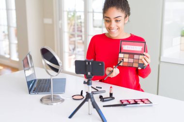 Genç afro-amerikan influencer kadın kayıt mutlu bir yüz ayakta ve dişleri gösteren kendinden emin bir gülümseme ile gülümseyerek öğretici makyaj