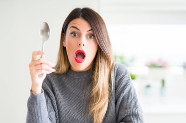 Genç, güzel bir kadın elinde gümüş kaşıkla evde. Şaşırmış bir yüzle korkmuş ve korku ifadesiyle heyecanlanmış.