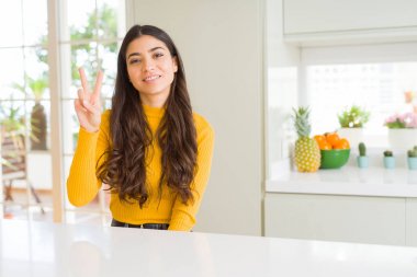 Genç güzel kadın evde beyaz masada gösteren ve parmakları ile işaret ederken iki numara kendinden emin ve mutlu gülümseyerek.