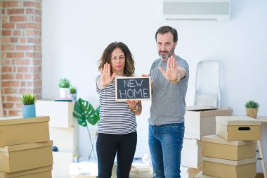 Orta yaş yaşlı çift ciddi ve kendinden emin ifade, savunma jesti ile dur işareti yapıyor açık el ile yeni bir eve hareket kara tahta tutan
