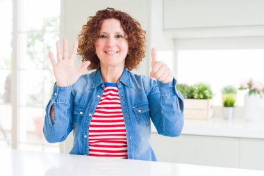 Kıvırcık saçlı orta yaş yaşlı kadın evde kot ceket giyen gösteren ve parmakları ile işaret ederken emin ve mutlu gülümseyerek altı numara.