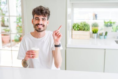 Sabahları kağıt bardakta kahve içen genç bir adam mutlu bir şekilde elini ve parmağını yana uzatır.