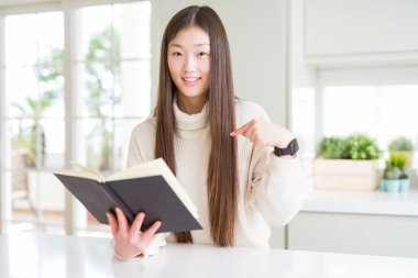 Güzel Asyalı kadın kendisine parmak işaret sürpriz yüzü ile bir kitap okuma