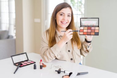 Güzel genç kadın makyaj kozmetik Renk palete duran ve diş gösterilen kendine güvenen bir gülümsemeyle gülümseyerek mutlu bir yüz ile uygulama kullanarak