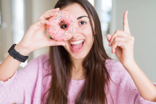 ピンクのチョコチップを食べる美しい若い女性ドーナツは 幸せな顔で指を指すアイデアや質問に驚きました ナンバーワン — ストック写真