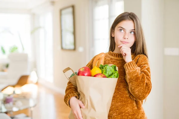 質問を考える新鮮な食料品の紙袋を持つ美しい若い女の子は 非常に混乱したアイデアを考えています — ストック写真