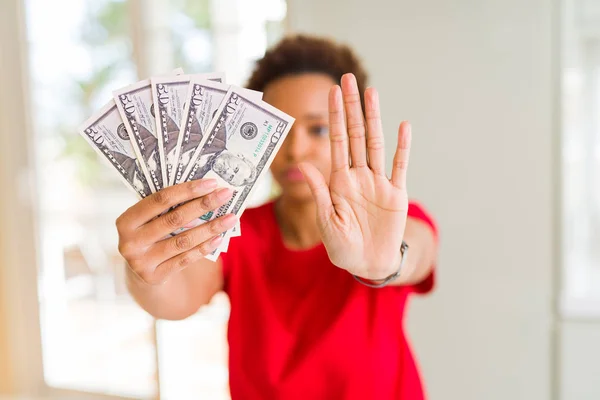 Young african american woman holding bank notes of fifty dollars with open hand doing stop sign with serious and confident expression, defense gesture