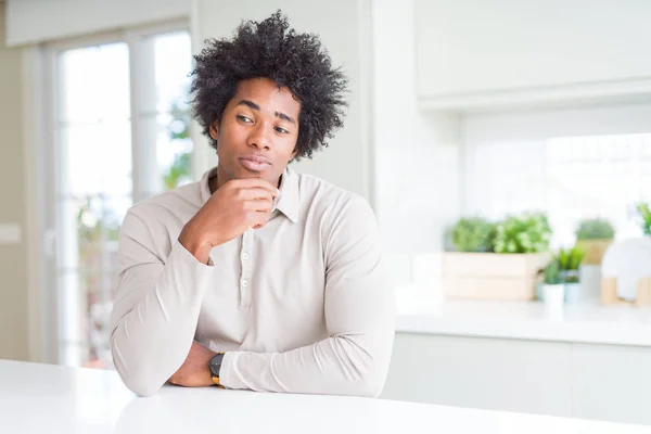 African American man at home looking confident at the camera with smile with crossed arms and hand raised on chin. Thinking positive.