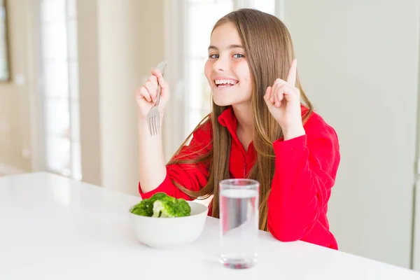 新鮮なブロッコリーと飲料水を食べる美しい若い女の子の子供は 幸せな顔で指を指すアイデアや質問に驚きました ナンバーワン — ストック写真