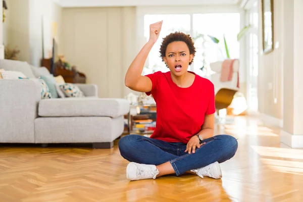 若い美しいアフリカ系アメリカ人の女性が怒って床の上に座っていると怒って怒って叫びながら拳をフラストレーションと激怒を上げる 激怒と積極的な概念 — ストック写真