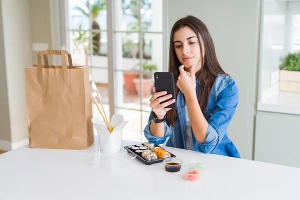 Beautiful young woman ordering food delivery from app using smartphone serious face thinking about question, very confused idea