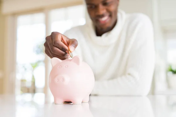 Handsome young african man putting a coin inside piggy bank smil