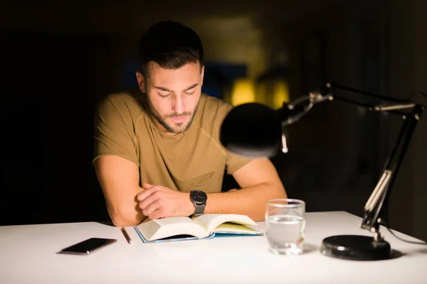 Joven hombre guapo estudiando en casa, leyendo un libro por la noche — Foto de Stock