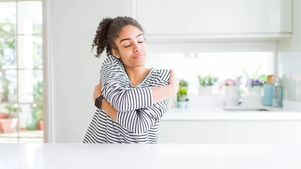 Beautiful african american woman with afro hair wearing casual striped sweater Hugging oneself happy and positive, smiling confident. Self love and self care