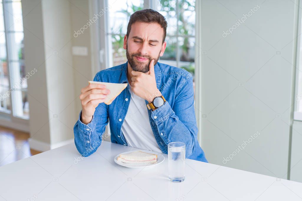 Handsome man eating healthy sandwich serious face thinking about question, very confused idea