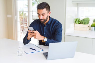 Yakışıklı İspanyol iş adamı ofiste akıllı yüz ciddi düşünme emin bir ifade ile akıllı telefon ve dizüstü bilgisayar kullanarak