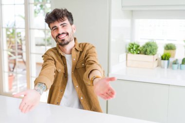 Sıradan bir ceket giymiş genç bir adam beyaz masada oturmuş kameraya bakıyor ve sarılmak için kollarını açmış gülümsüyor. Mutluluğu kucaklayan neşeli bir ifade..
