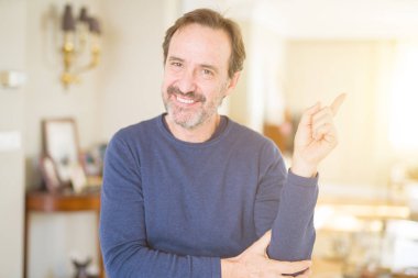 Kameraya bakarak yan el ve parmak ile işaret eden yakışıklı orta yaş erkek evde yüzünde kocaman bir gülümseme ile.