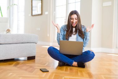 Güzel genç kadın dizüstü bilgisayar kullanarak çapraz bacaklar ile katta oturan çok mutlu ve heyecanlı, kazanan ifade büyük bir gülümseme ile çığlık zafer kutluyor ve ellerini kaldırdı
