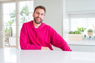 Evde rahat sweatshirt giyen ve olumlu gülümseyen yakışıklı adam