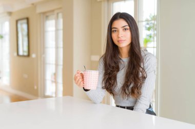 Bir fincan kahve içen genç bir kadın, kendine güvenen bir ifadeyle akıllı bir yüzle ciddi düşünüyor.