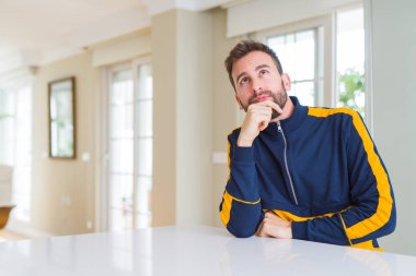 Yakışıklı adam evde elleri çenesi ile soru, dalgın ifade düşünüyor. Düşünceli bir yüzle gülümsüyor. Şüphe kavramı.