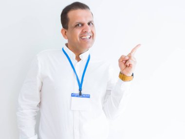 Beyaz arka plan üzerinde kimlik kartı takan orta yaş iş adamı yüzünde büyük bir gülümseme ile, kameraya bakarak yan el ve parmak ile işaret.