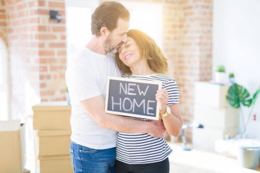 Orta yaş Senior çift yeni bir eve hareket, yeni bir ev metin ile bir tahta tutan Apartmant aşık mutlu gülümseyen