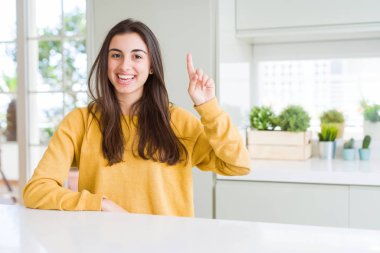 Sarı kazak giyen güzel genç kadın, kendinden emin ve mutlu gülümserken bir numaralı parmakla işaret ediyor..