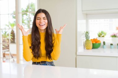 Genç güzel kadın evde beyaz masada deli ve deli kollarını kaldırdı ve kapalı gözleri heyecan çığlık ile başarı için deli kutluyor. Kazanan kavramı