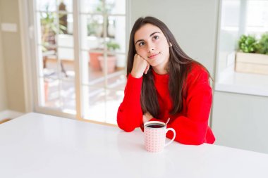 Güzel genç kadın bir fincan siyah kahve içerken çenesi üzerinde eliyle soru, dalgın ifade yi düşünüyor. Düşünceli bir yüzle gülümsüyor. Şüphe kavramı.