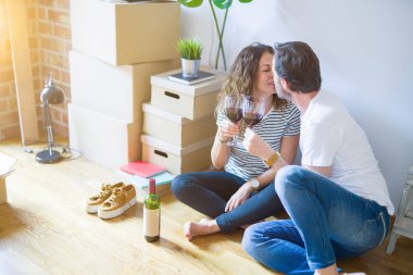 Orta yaş Senior romantik çift aşk yeni bir eve taşımak için mutlu gülümseyen bir bardak şarap içme kutluyor, etrafında kutuları ile daire katında oturan