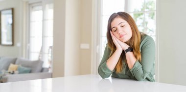 Evde uyuyan güzel genç kadın yorgun rüya ve kapalı gözlerle gülümseyerek birlikte elleri ile poz.