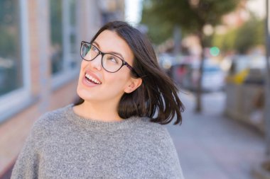 Genç güzel kadın gözlük giyerek şehir kasabasında sokakta emin yürüyüş gülümsüyor