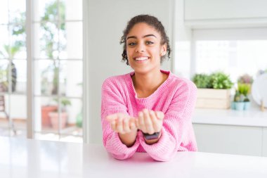 Afro saçlı güzel afro-amerikan kadın rahat pembe kazak birlikte alma veya jest veren avuç içi ile gülümseyerek. Tutma ve koruma