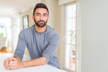 Yakışıklı İspanyol adam yüzünde ciddi ifade ile evde rahat sweatshirt giyiyor. Kameraya basit ve doğal bir bakış.