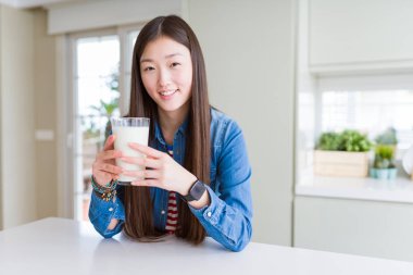 Güzel Asyalı kadın ayakta mutlu bir yüz ile süt taze bir bardak içme ve dişleri gösteren kendinden emin bir gülümseme ile gülümseyerek